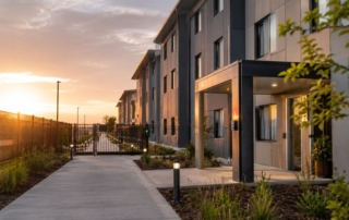 Photograph of a modern purpose-built worker dormitory exterior at sunrise, showing clean walkways