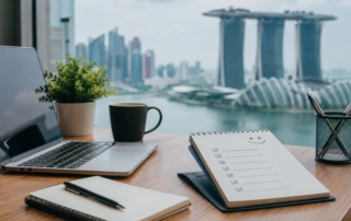 Photo of a professional Singapore remote-work setup (laptop, notebook, Singapore skyline in background) with friendly onboarding checklist visible