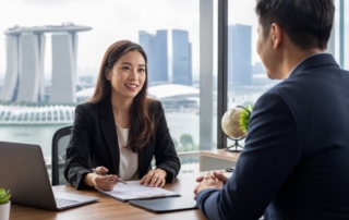 A professional meeting between an HR manager and a recruitment consultant in an office, with Singapore skyline visible t