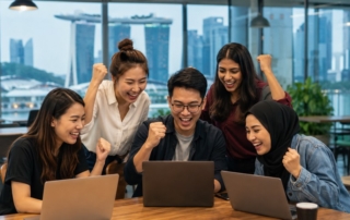 An 800x600 image of a diverse group of bootcamp graduates celebrating with laptops in a modern Singapore co-working spac