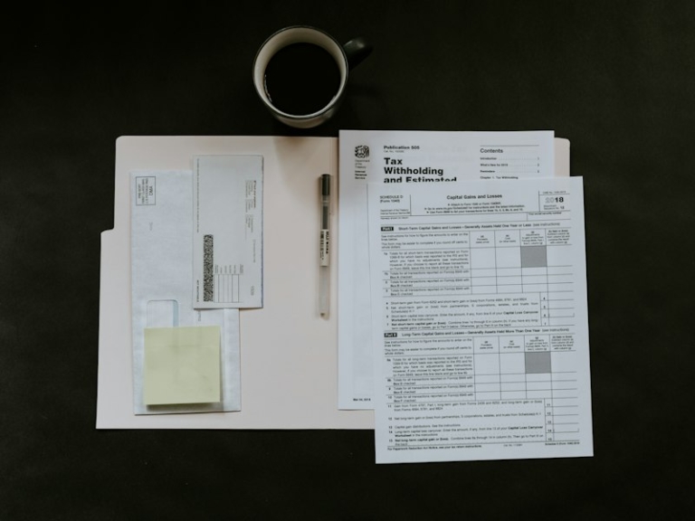 Tax forms, a pen and a coffee mug on a dark desk