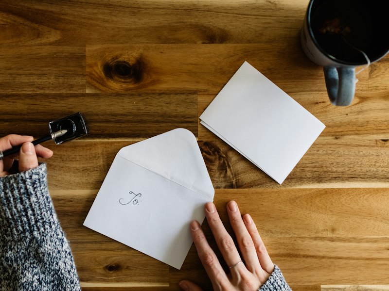 A person writing a letter on paper at a desk beside a cup of coffee
