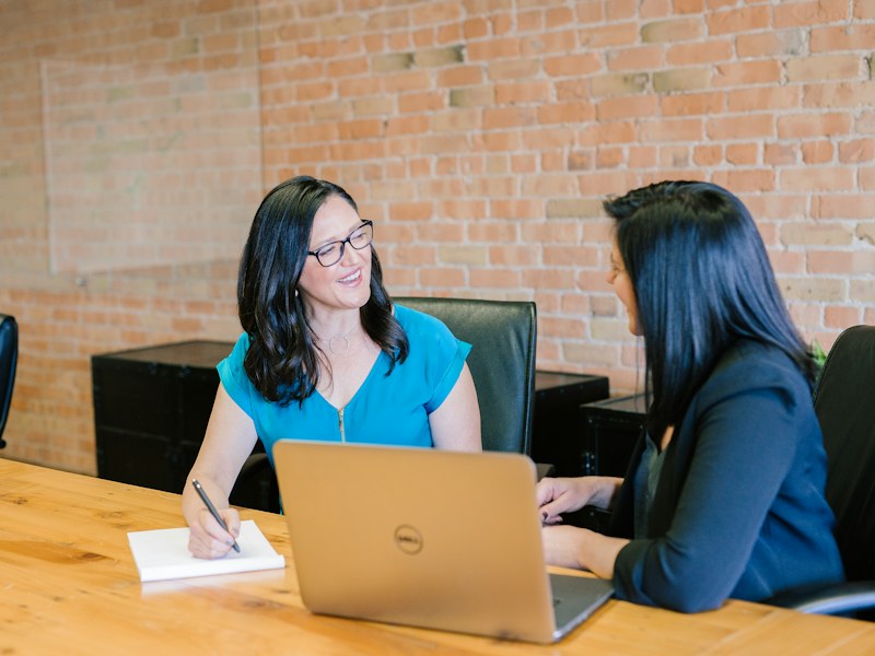 HR interviewer taking notes across a table from a job candidate, with a laptop between them